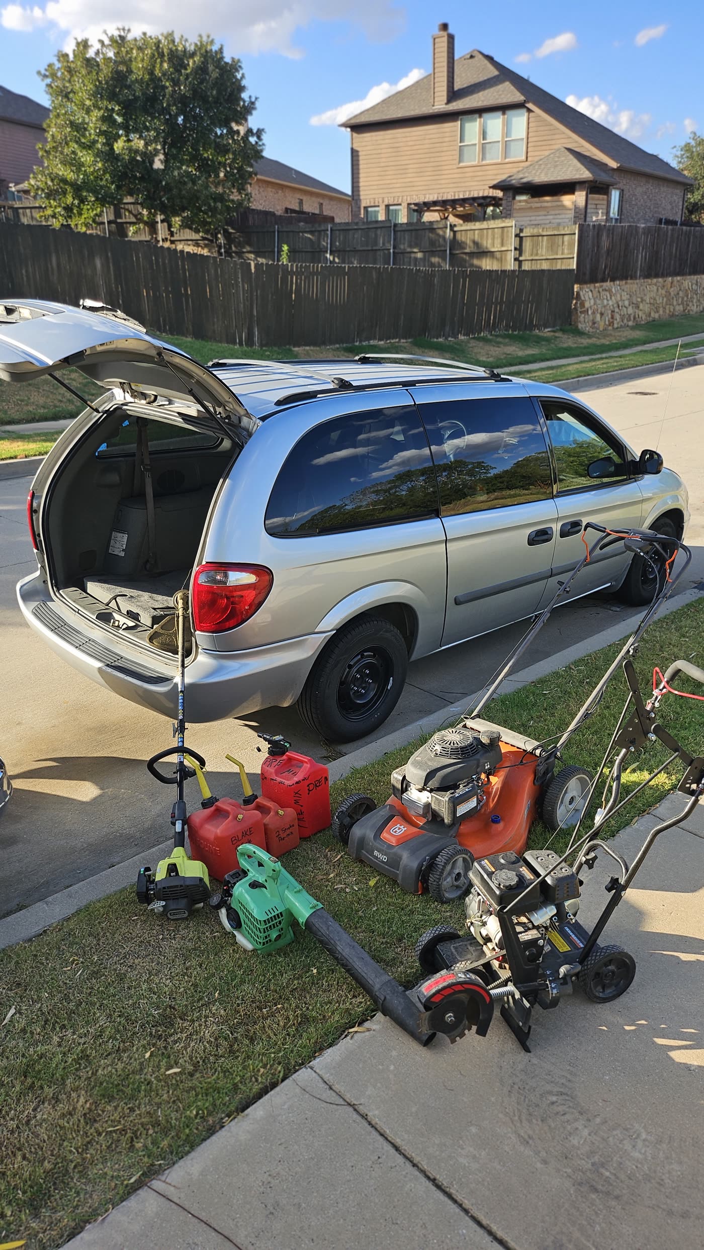 Lawn equipment staged beside the work van: Husqvarna mower, edger, trimmer, blower, and fuel cans